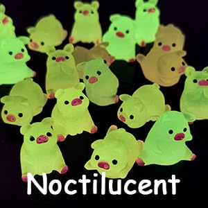Multiple glow-in-the-dark plastic figurines shaped like small ghosts or blob creatures with simple faces, arranged on a dark background. The figurines are primarily light green in color.