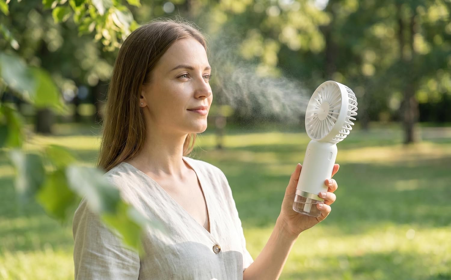 Woman outdoors holding white handheld electronic device with circular vents, appearing to be a portable cooling or air quality device in natural garden setting.